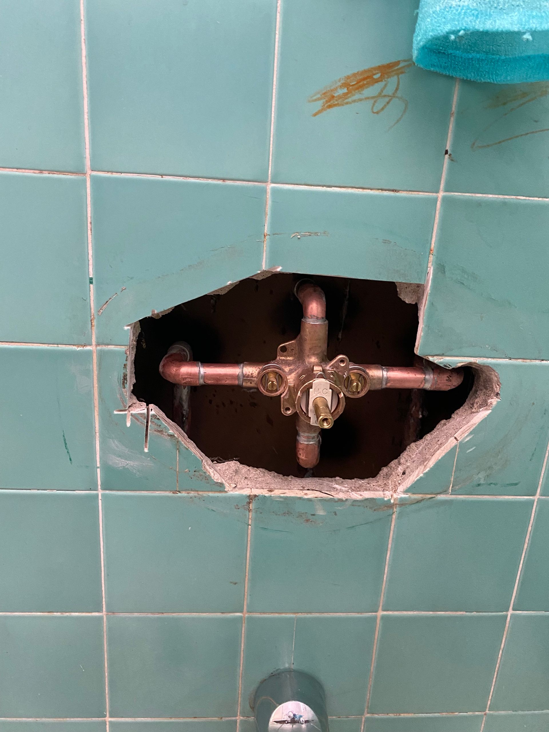 A hole in a tiled wall with a copper pipe in it