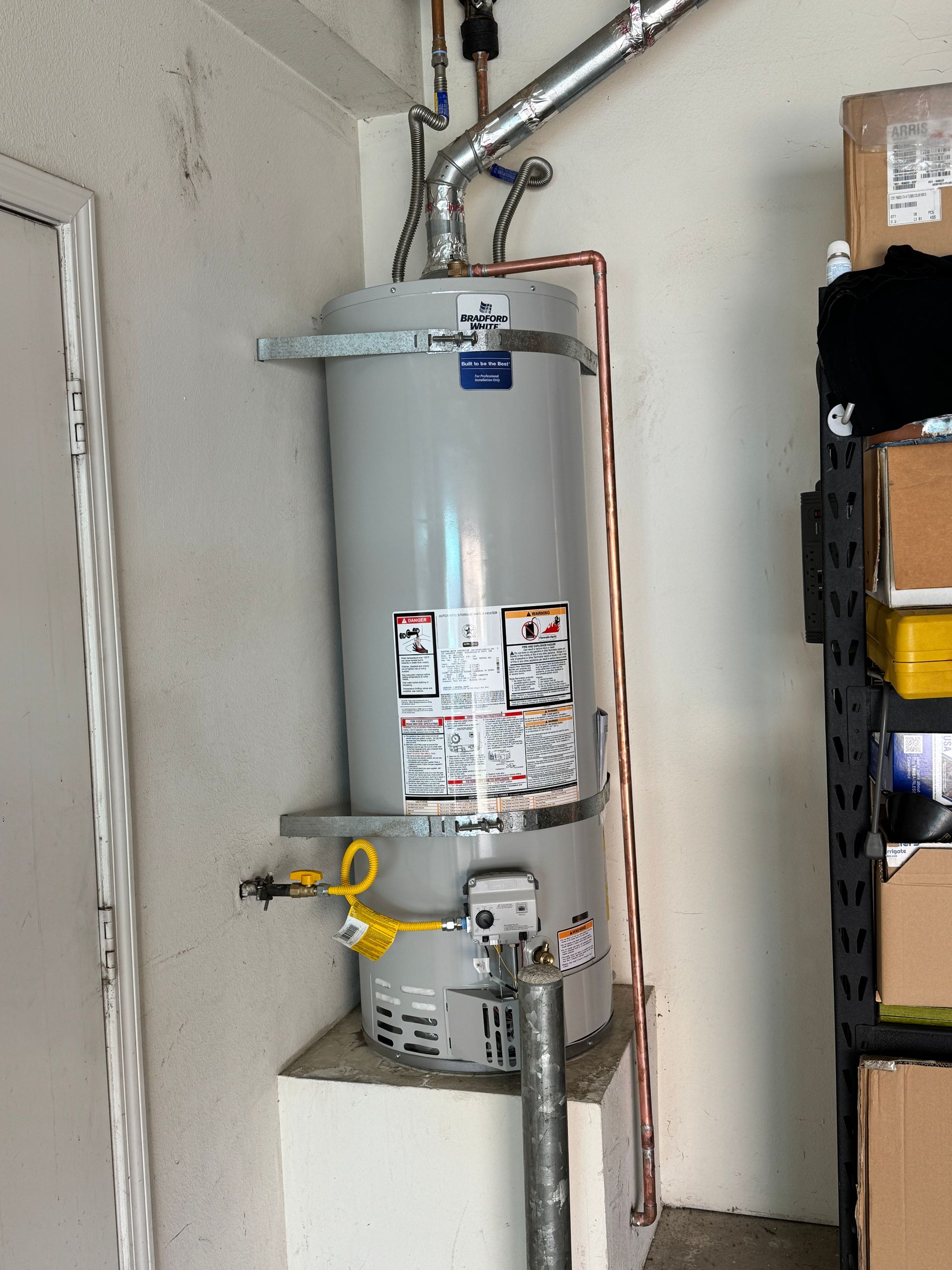 A water heater is sitting on top of a concrete block in a garage.