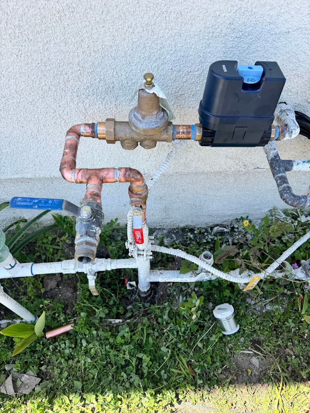 A water meter is attached to a pipe outside of a house.