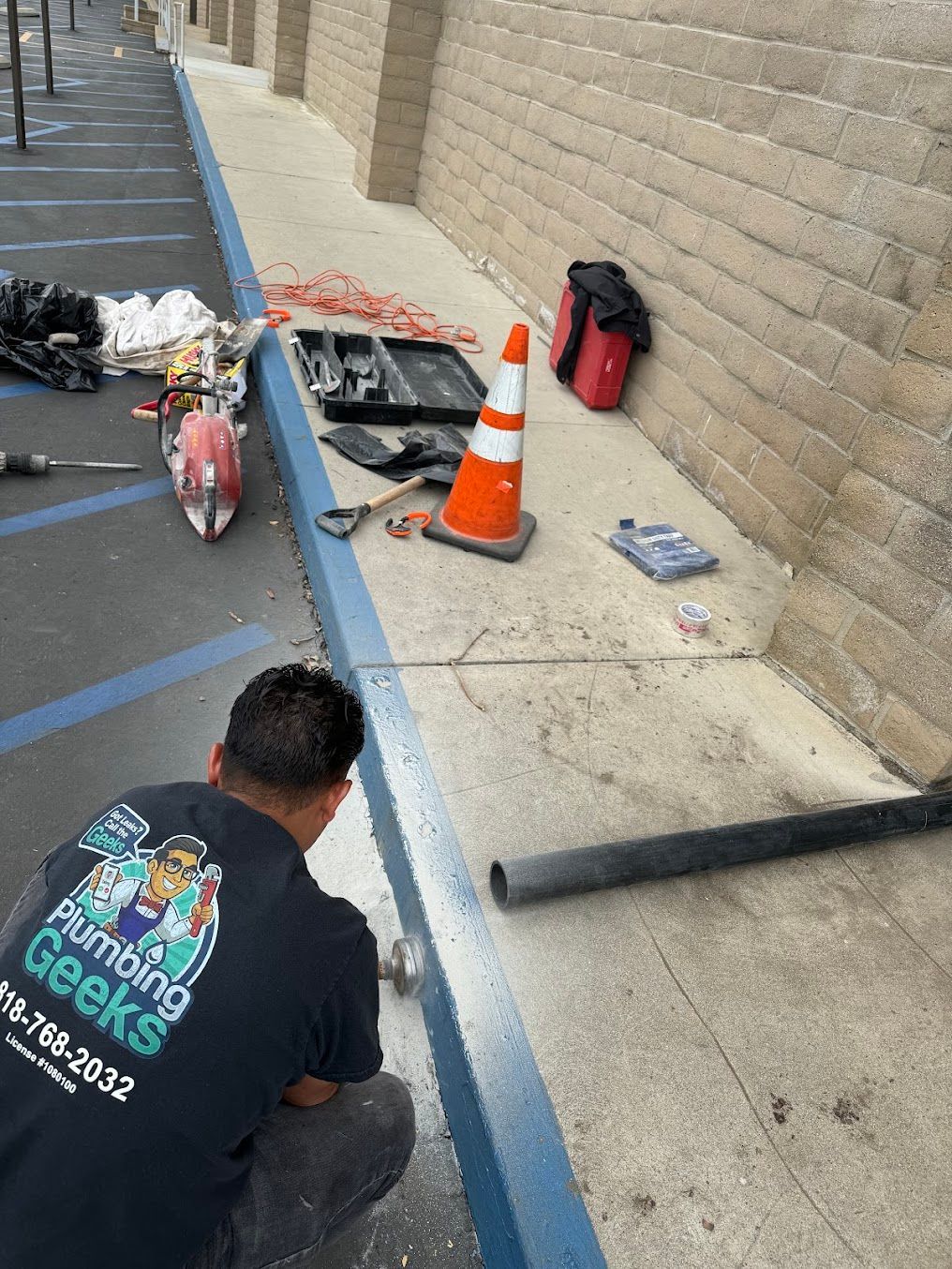 A man is working on a sidewalk next to a brick wall.