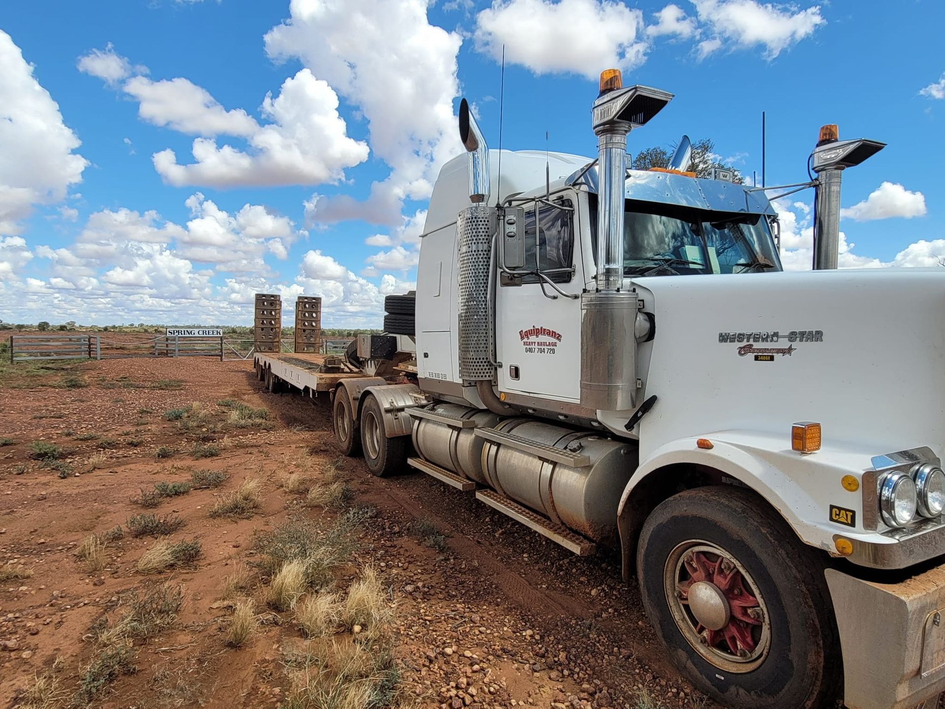 A white semi truck is parked in the middle of a dirt field.