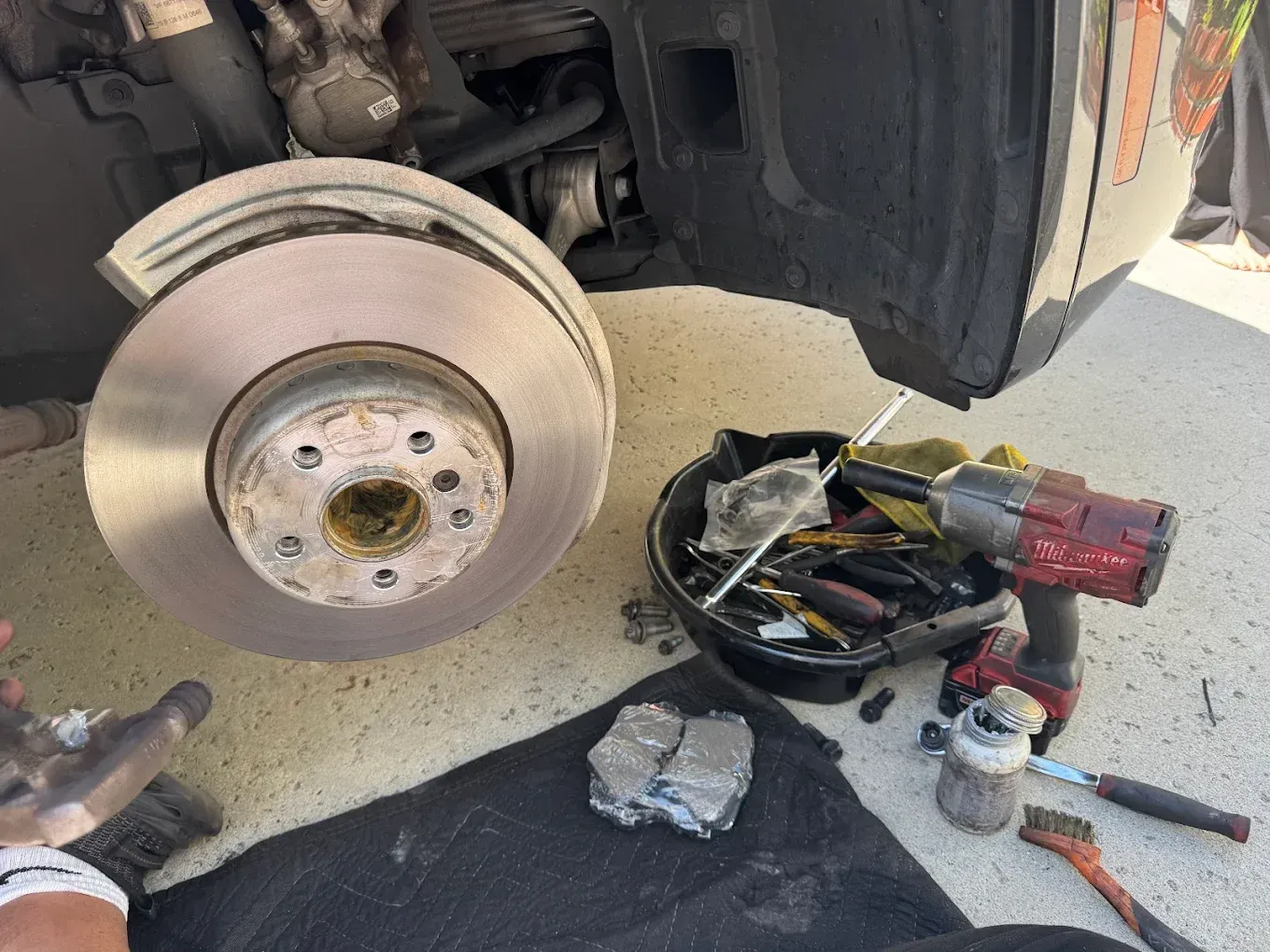 Car brake rotor and pads removed, tools and parts visible on the ground.