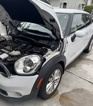 White Mini Cooper with hood open, parked on concrete.