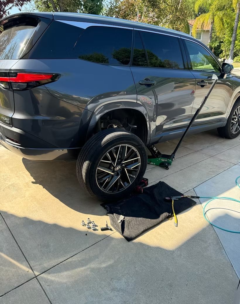 Dark SUV with a flat tire, being worked on with a jack and tools on a driveway.
