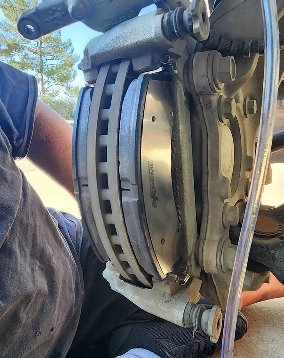Person replacing brake pads on a vehicle. The caliper, rotor, and new brake pads are visible.