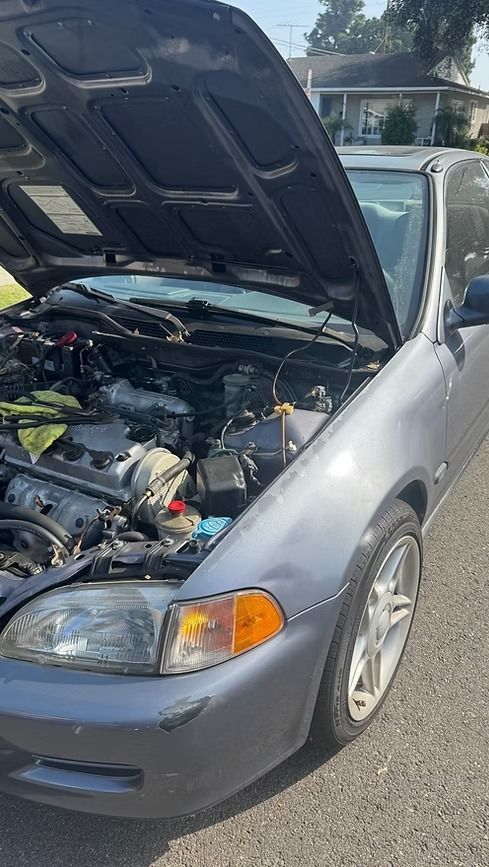 Gray car with hood open, revealing engine components. Daylight setting.