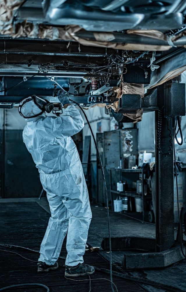 Person in protective suit welding under a vehicle lifted on a hoist in a workshop. Sparks are visible. — Pelican Motors Service Centre in Caloundra West, QLD