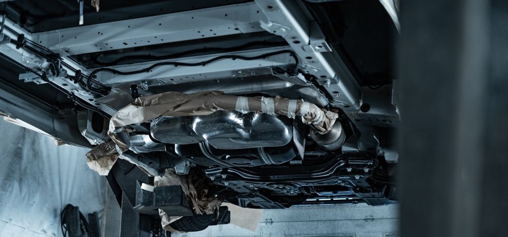 Underside of a vehicle. Exhaust pipes, metal undercarriage components, and wiring are visible. — Pelican Motors Service Centre in Caloundra West, QLD