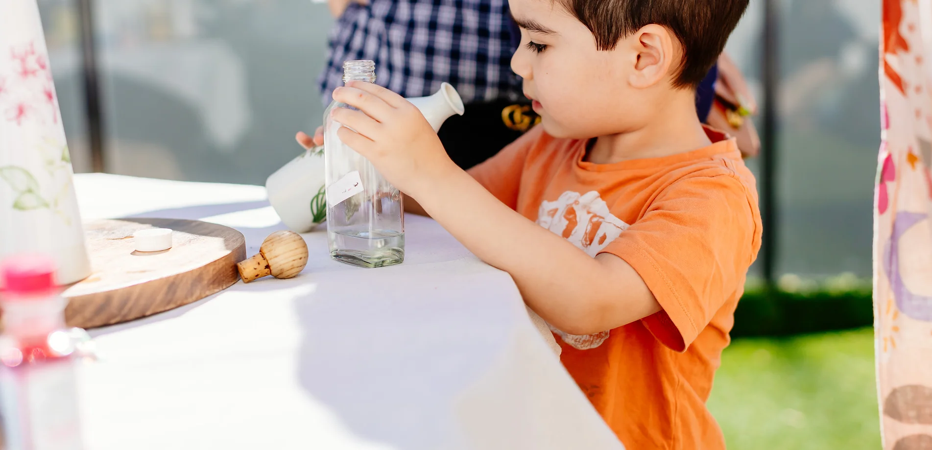 a young boy is sitting at a table drinking from a bottle .