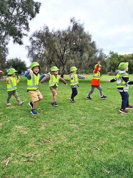 a group of children wearing hard hats and safety vests are playing in a park .