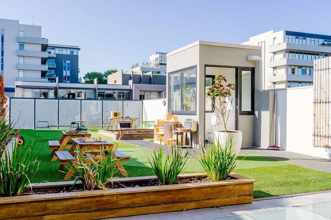 a rooftop garden with tables and benches and a building in the background .