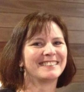 Smiling woman with brown hair in front of a wooden wall