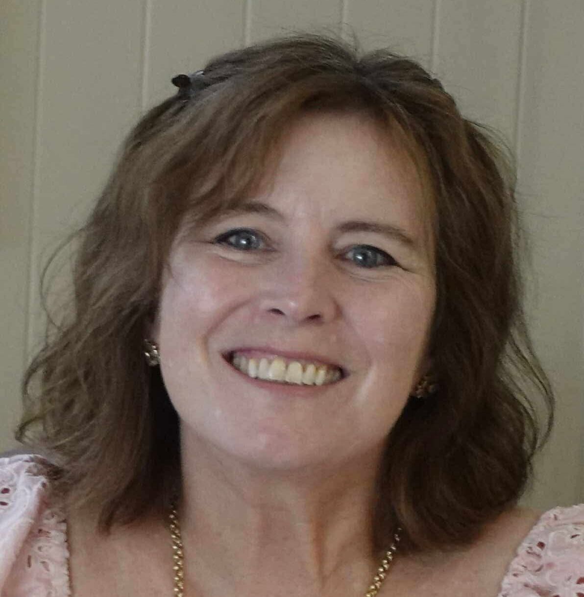 Smiling woman with brown hair in front of a wooden wall