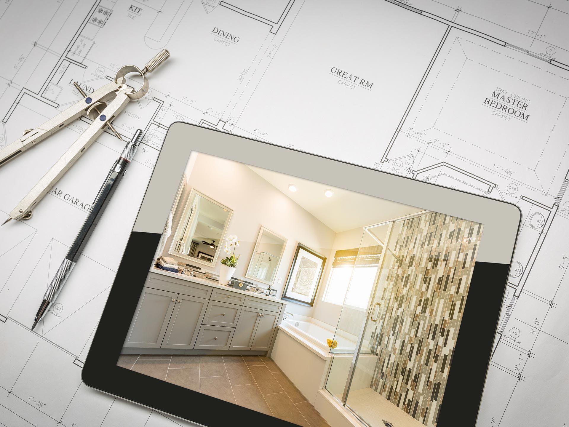 Tablet showing a bathroom remodel photo on top of home blueprints with tools. Tablet showing a bathroom remodel photo on top of home blueprints with tools.