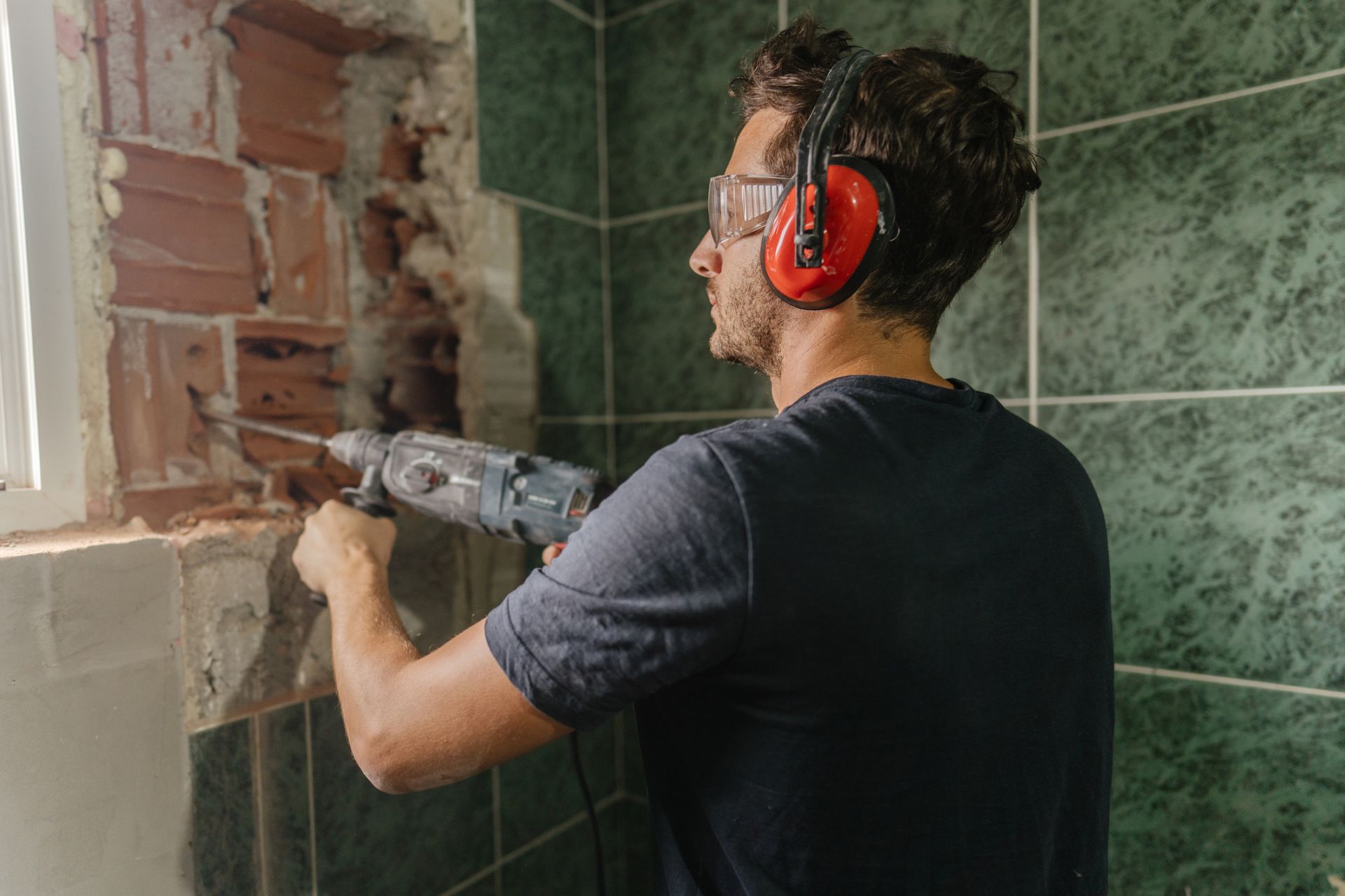 A worker wearing glasses uses a power drill while working on a bathroom remodeling project. A worker wearing glasses uses a power drill while working on a bathroom remodeling project.