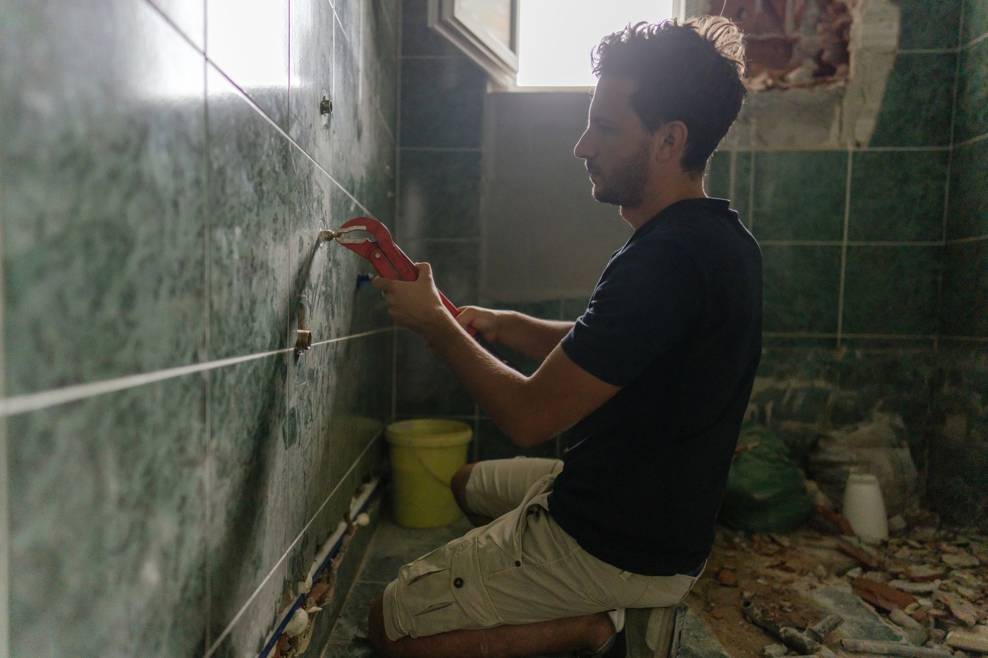 A worker uses a wrench while working on the plumbing during a bathroom remodeling project.
