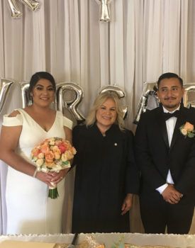 A bride and groom are posing for a picture with a wedding officiant.