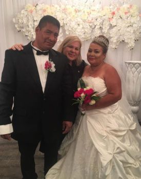 A bride and groom are posing for a picture with a woman in a wedding dress.