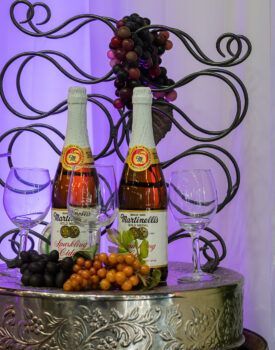 Two bottles of martinellis sparkling wine are sitting on a table with grapes and wine glasses