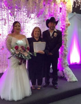 A bride and groom are posing for a picture with a judge at their wedding ceremony.