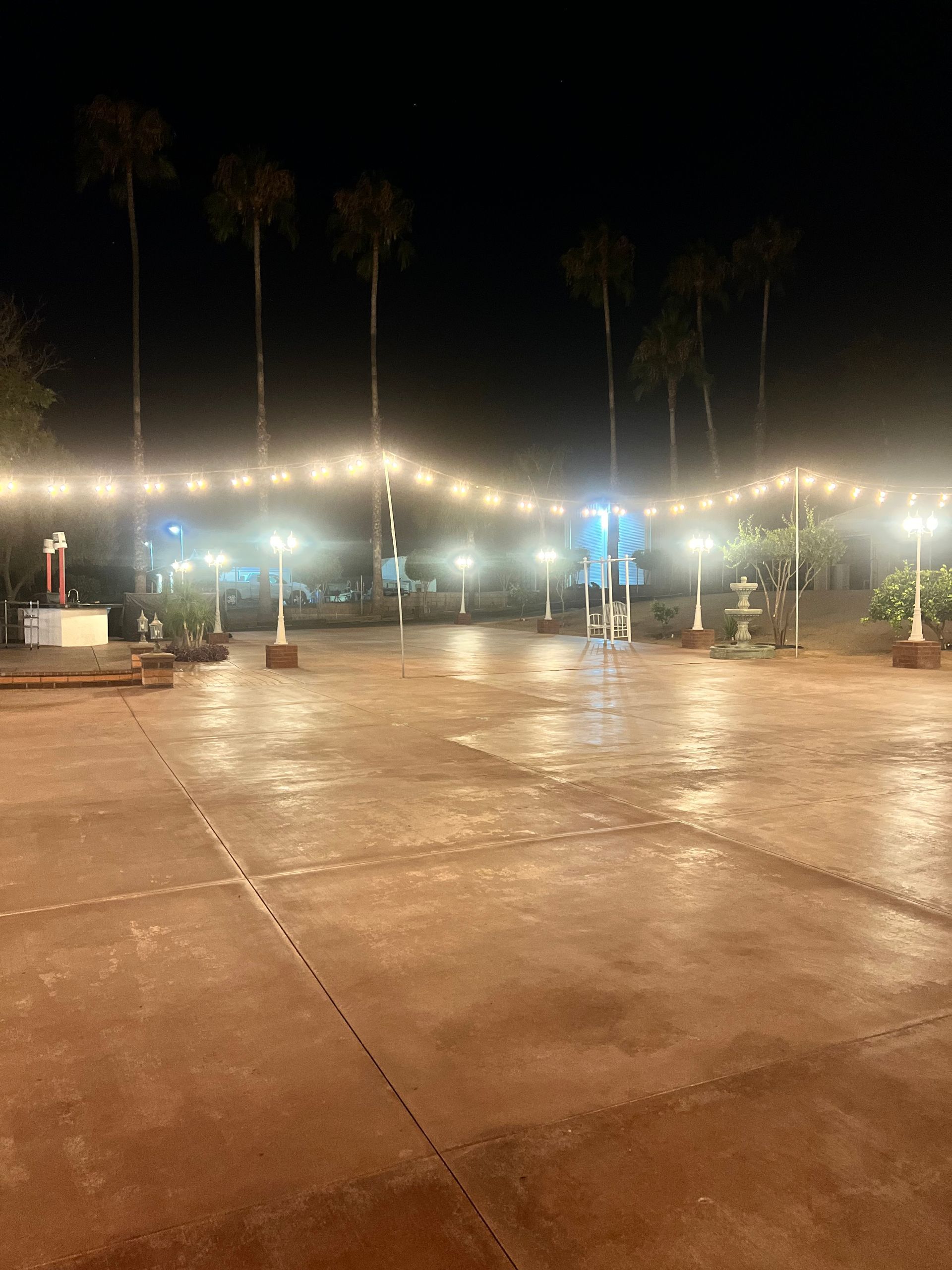 A large empty parking lot is lit up at night with palm trees in the background.