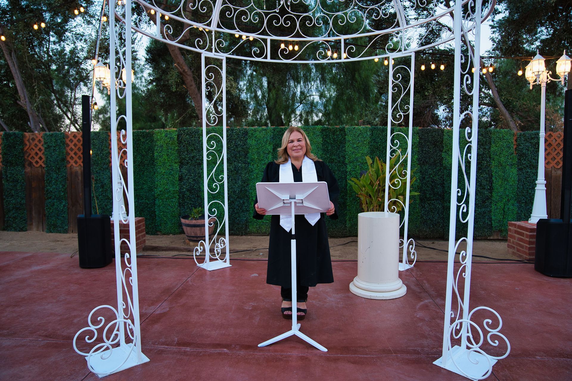 A woman in a black dress is standing in front of a wall of flowers.