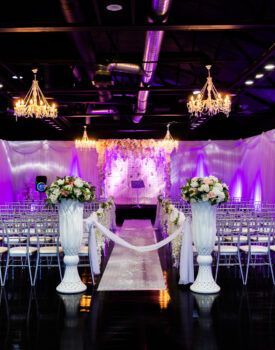 A wedding ceremony is taking place in a large room with purple lights.