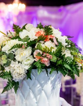 A white vase filled with white flowers and greenery is on a table.