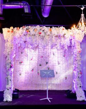A stage with a podium in front of a wall of flowers.