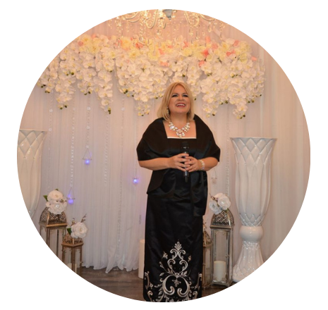 A woman in a black dress is standing in front of a wall of flowers.