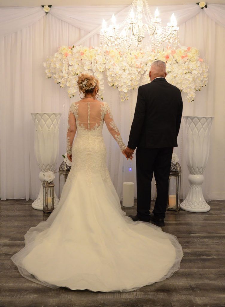 A bride and groom are holding hands in front of a chandelier.