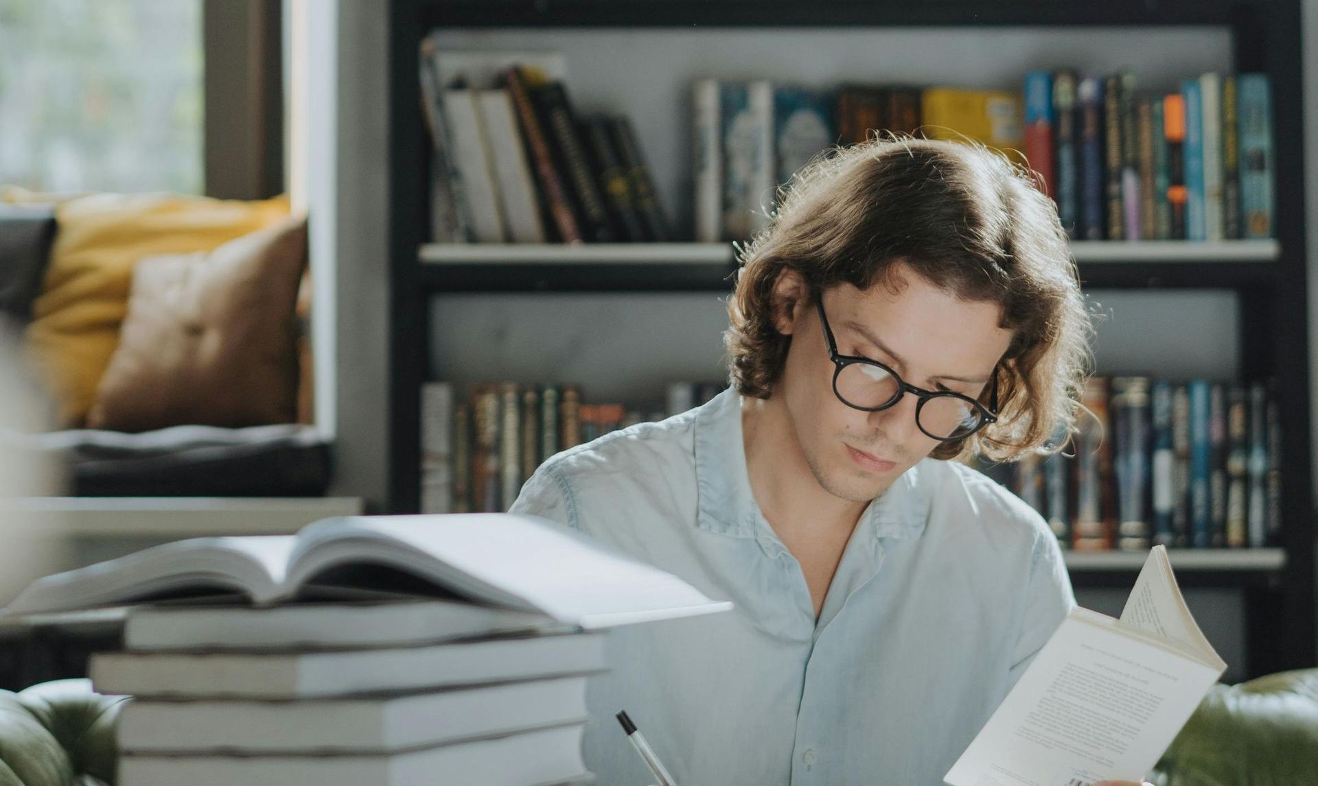 Een man met een bril leest een boek in de bibliotheek.