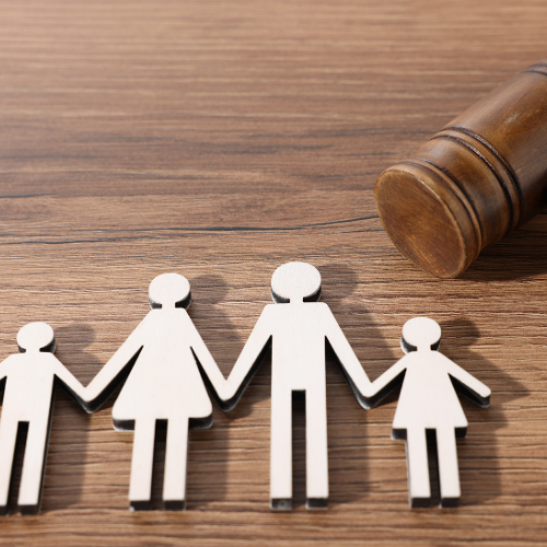 Wooden family figures holding hands beside a gavel on a wooden surface.