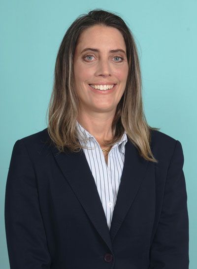 Woman in navy blazer and striped shirt smiles in front of a blue backdrop.