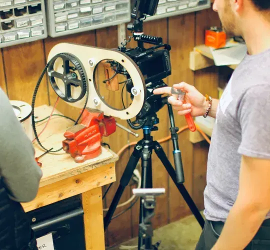 a man stands in front of a camera while another man looks on