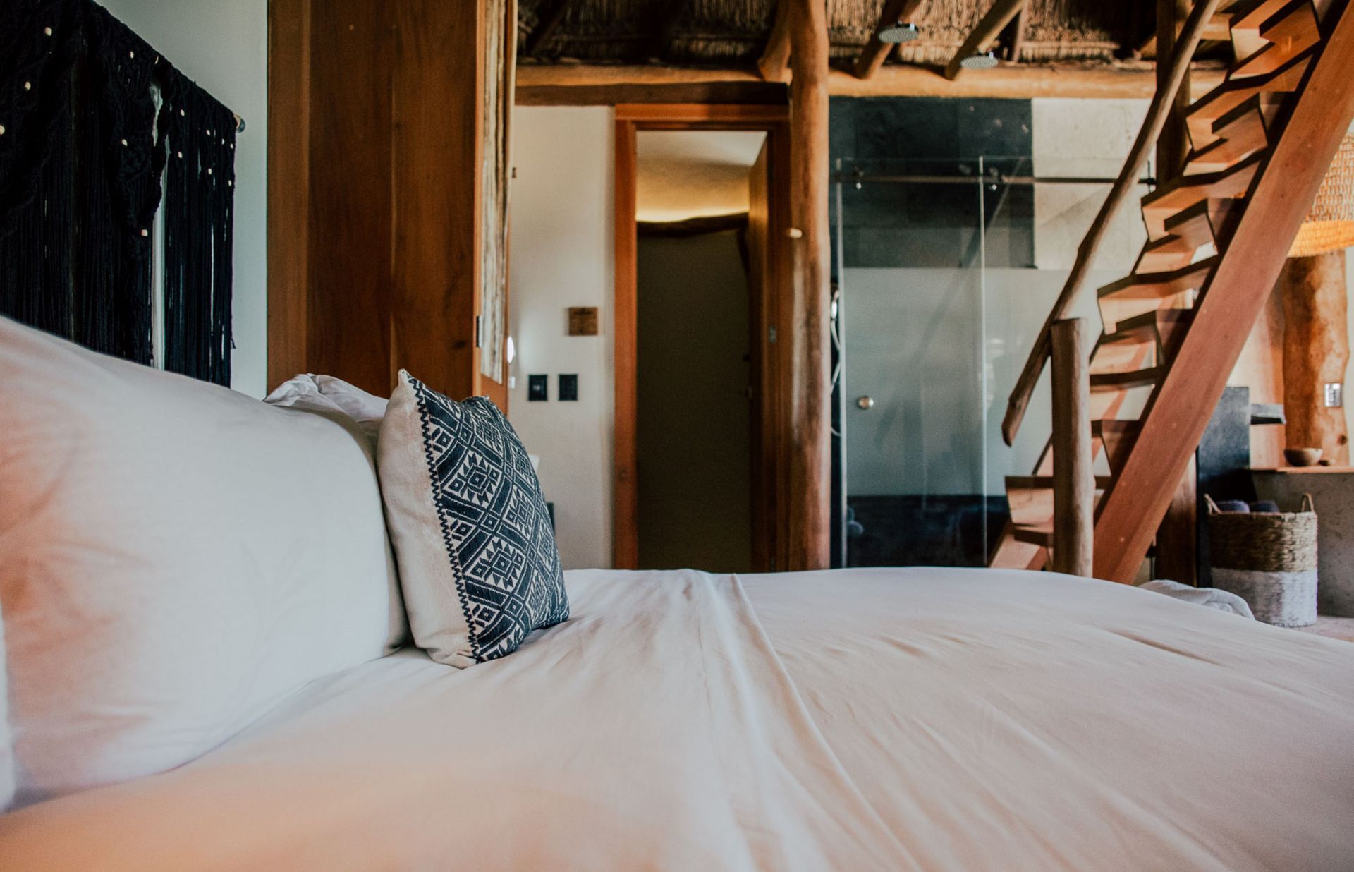Bedroom with white bedding, decorative pillow, wooden stairs, and open doorway.