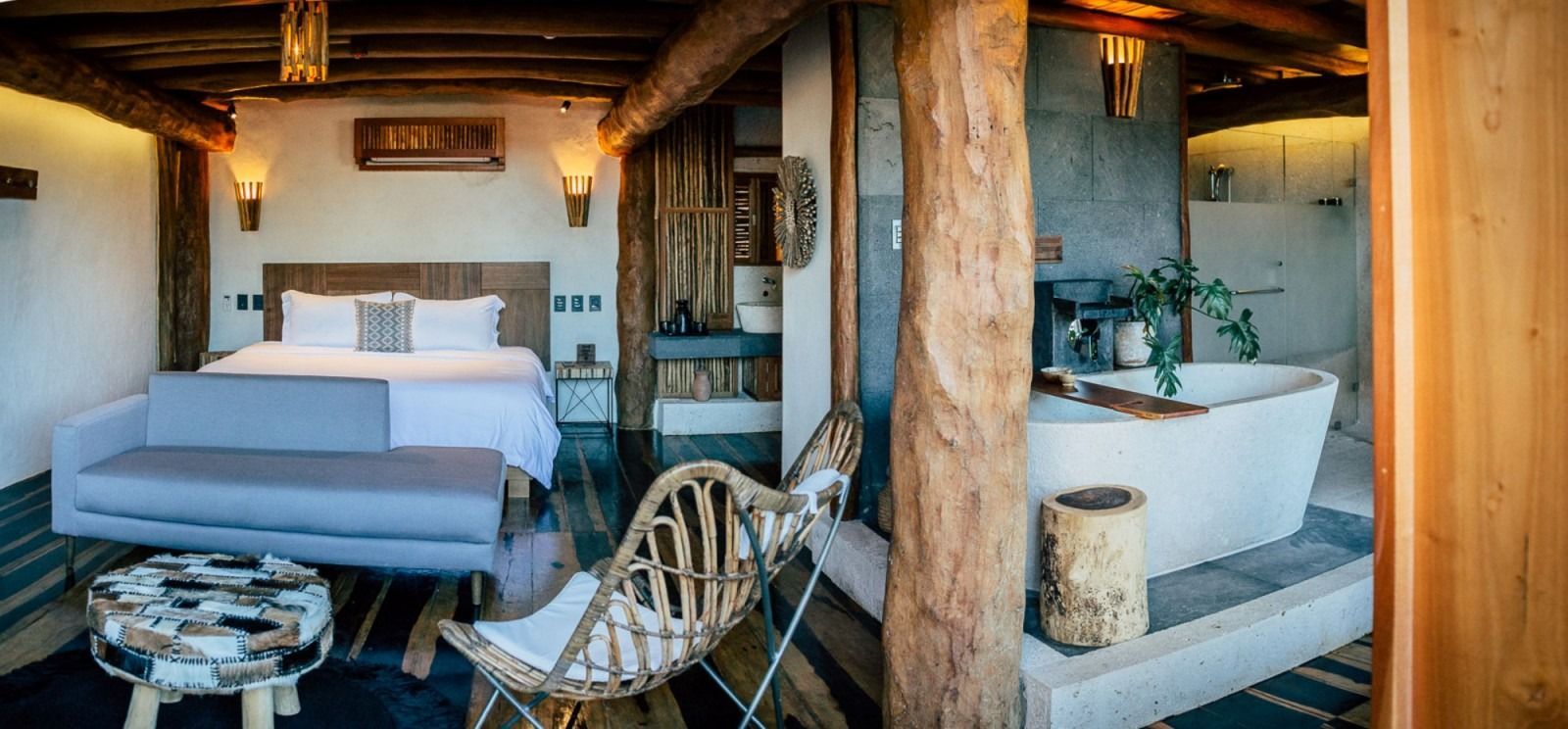 Rustic hotel room with a bed, couch, bathtub, and wood beams.