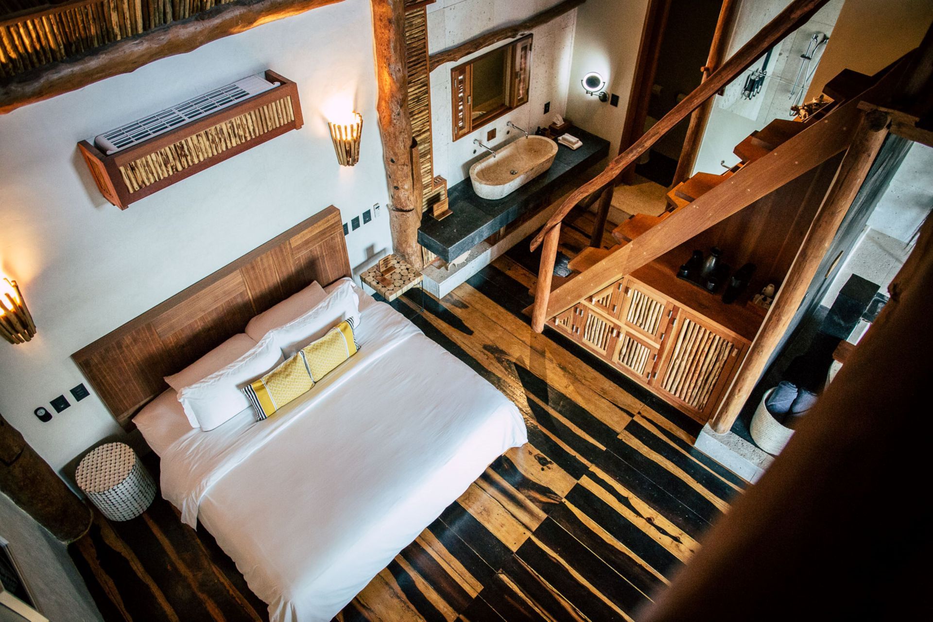 Bedroom with wooden beams, platform bed, and bathroom with sink; overhead view.