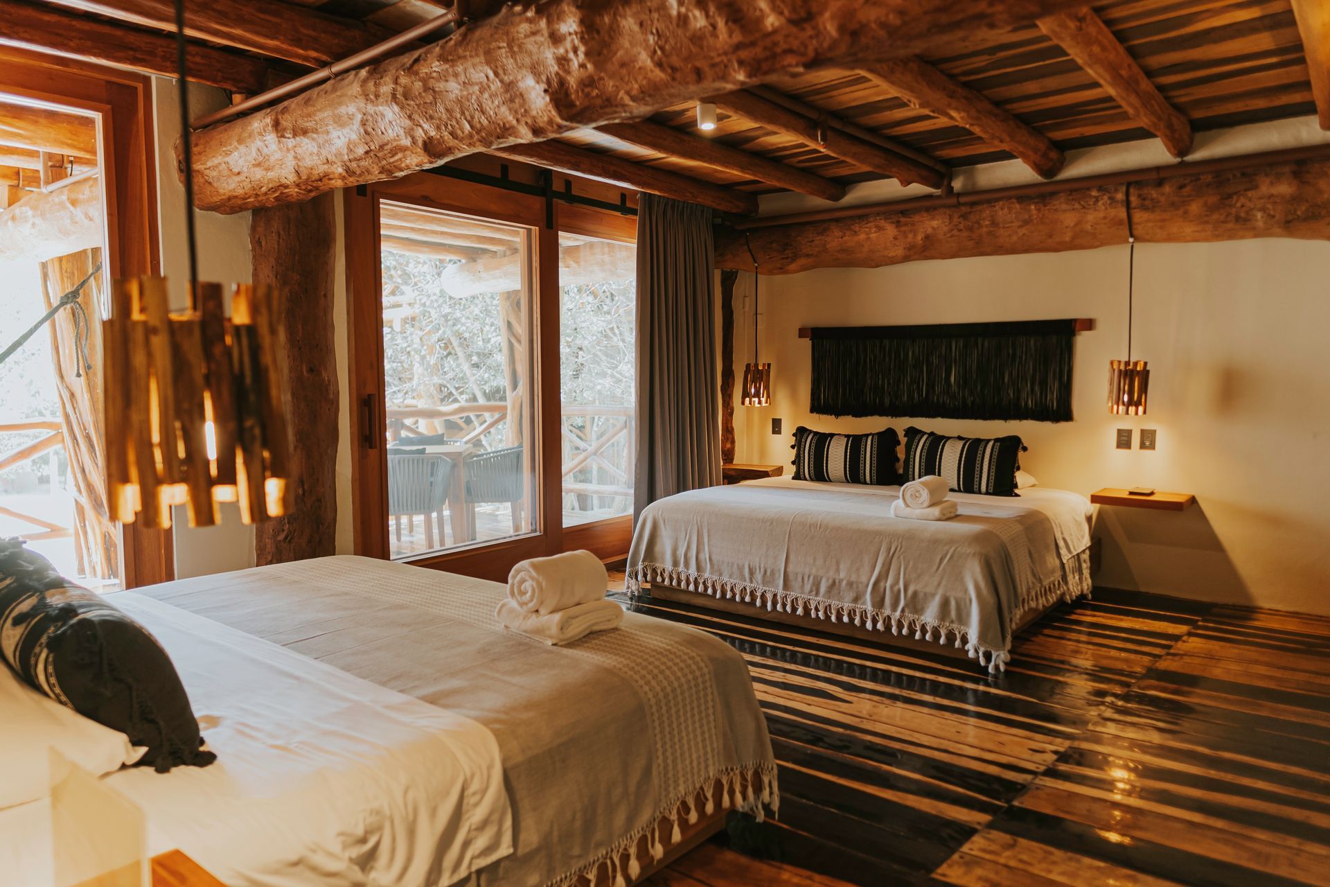 Bedroom with two beds, wooden beams, large windows, and rustic decor.