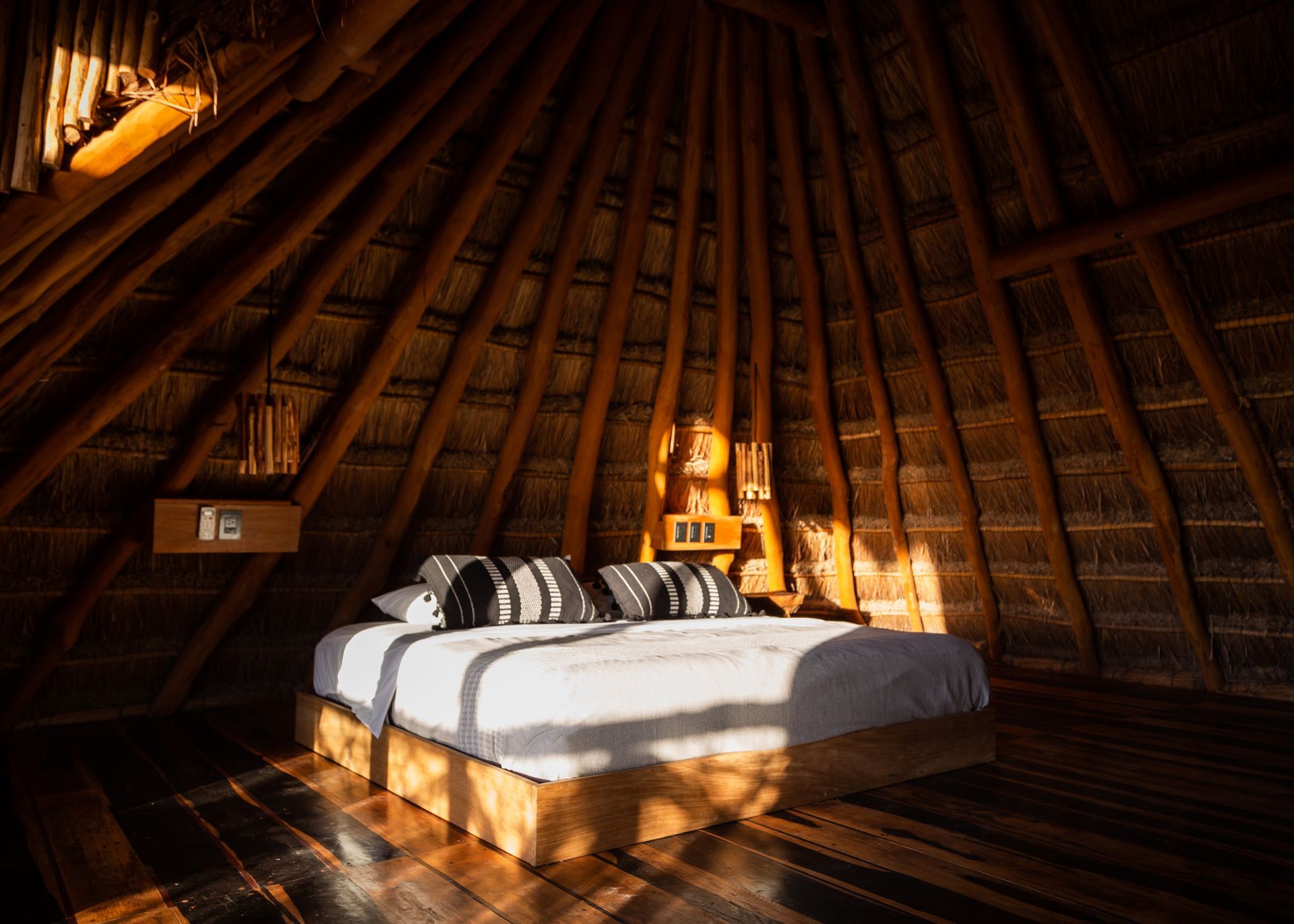 Bedroom with thatched roof, wooden bed, and sunlight.