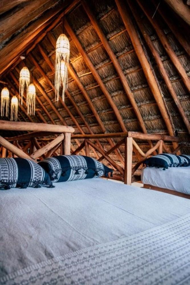 Loft bedroom with thatch roof, wooden beams, beds with white linens, black and white pillows, and hanging lights.