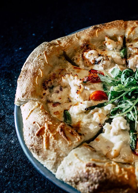 Pizza with creamy sauce, cherry tomatoes, and arugula on a plate.