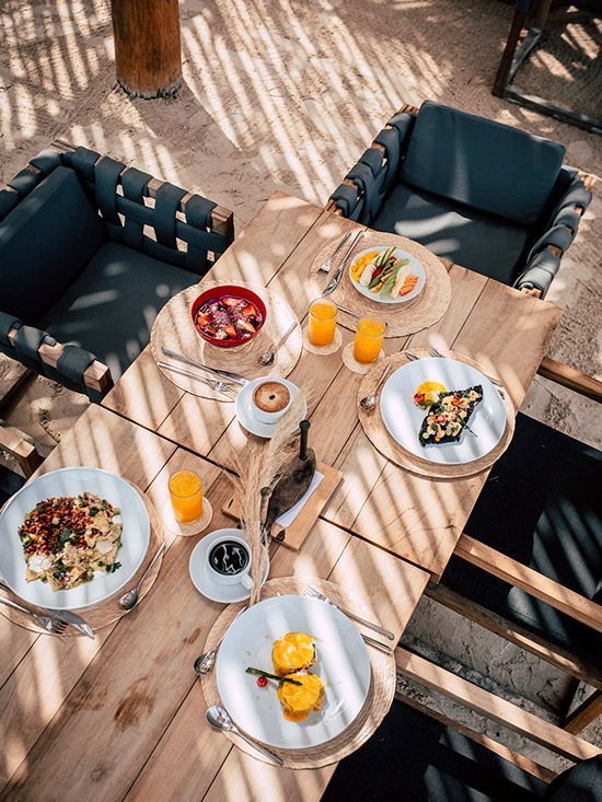 Breakfast table set with plates, orange juice, and coffee; outdoor dining with shadow patterns.