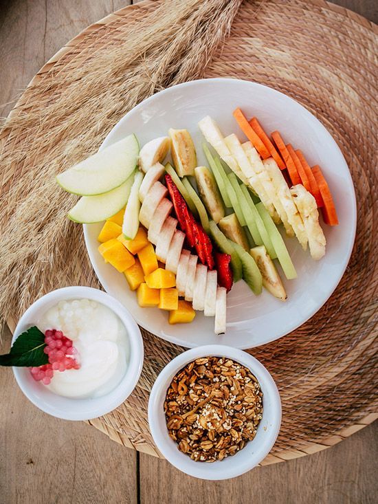 Fruit and vegetable platter with yogurt and granola in bowls.