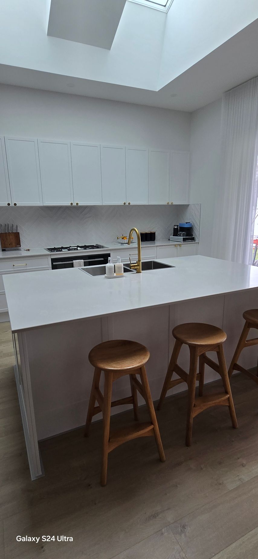 A clean kitchen space with white kitchen island and wooden stools — A Place 2 Shine In Chisholm, NSW