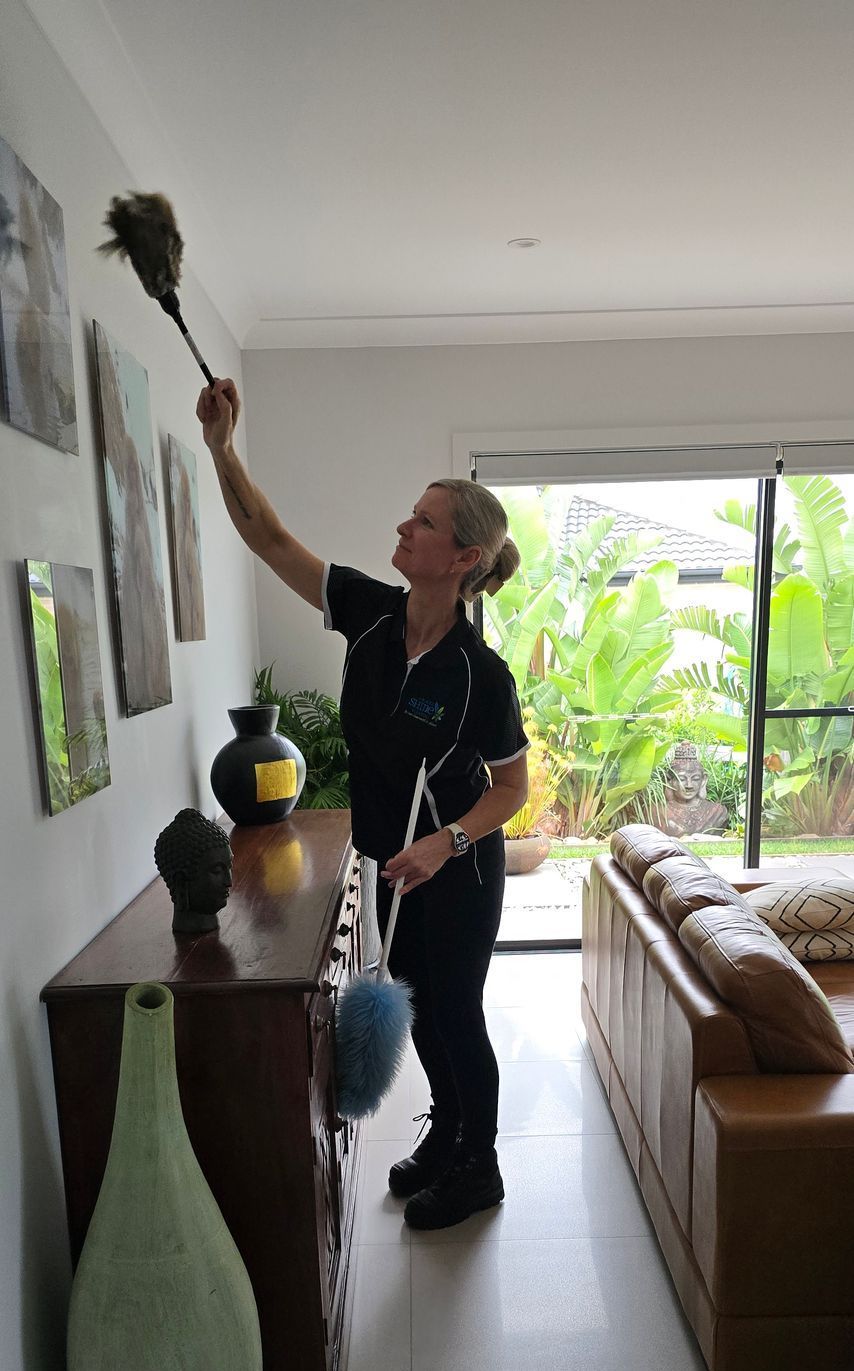 A Woman is dusting images on a wall— A Place 2 Shine In Chisholm, NSW
