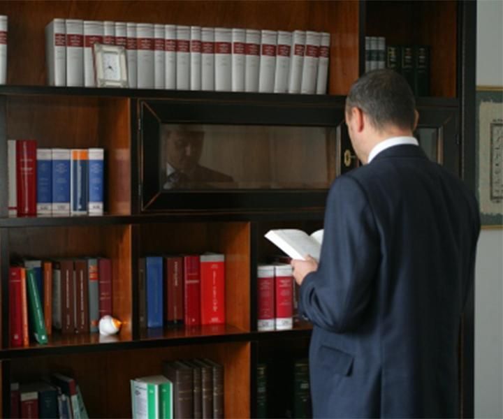Un uomo in giacca e cravatta legge un libro davanti a una libreria piena di testi giuridici.