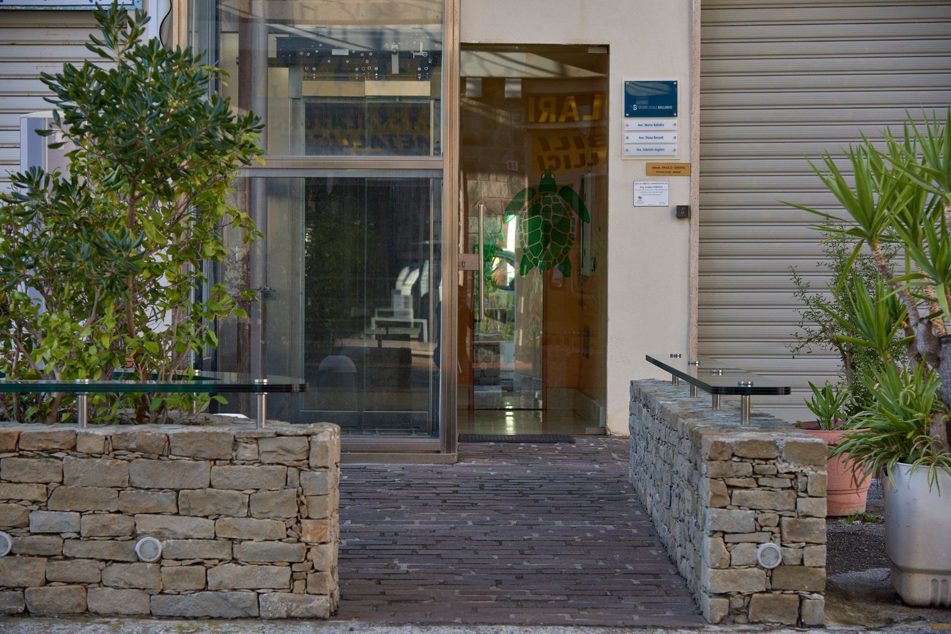 Ingresso con fioriere in mattoni, porta in vetro e rampa in legno.