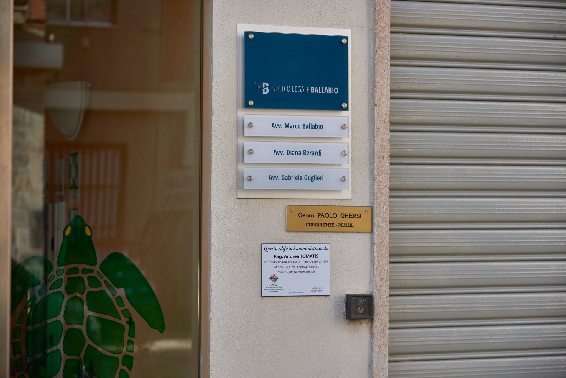 Cartello con nomi in testo bianco sulla parte esterna di un edificio con una tartaruga e una porta di metallo chiusa.