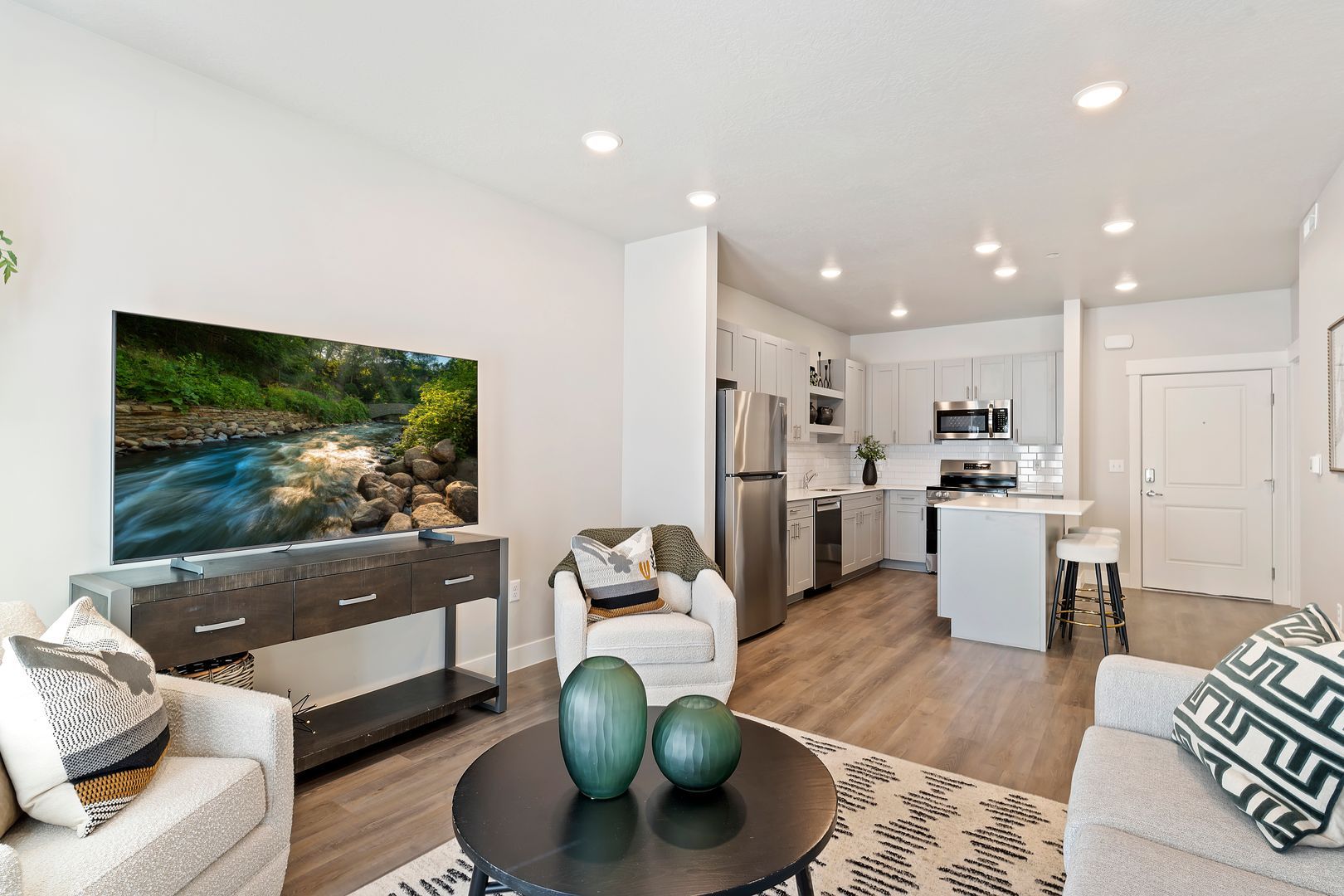 Living room with open kitchen. TV on console, two armchairs, a rug and a coffee table.